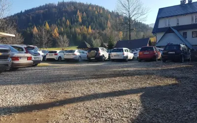 Parking w Kuźnicach, jesienny las na wzgórzu, rząd samochodów na żwirowym placu.
