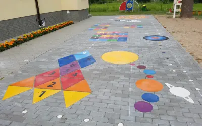 Kolorowe gry plenerowe na placu zabaw: rakieta z liczbami, układ planet i plansza do gry.