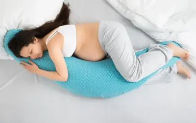 Mujer embarazada duerme de lado, abrazando una almohada de apoyo. Las posturas de dormir en el embarazo son clave para el descanso.