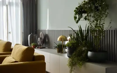 Musztardowe fotele i zielone rośliny ożywiają wnętrze. Jaki kolor pasuje do popielu? Złoto lampki i dekoracji dodaje elegancji.