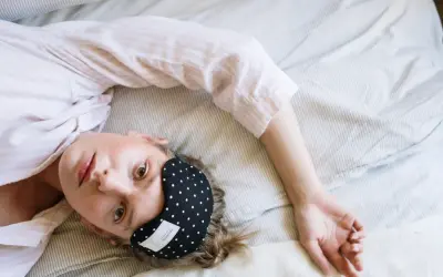 Kobieta w piżamie leży na łóżku z opaską na oczy, marząc o spokojnym śnie, jak po zażyciu zolpidemu.