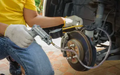 Mechanik odpowietrza hamulce, sprawdzając objawy zapowietrzenia układu. Widać narzędzie z manometrem podłączone do zacisku hamulcowego.