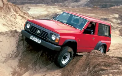 Czerwony Nissan Patrol Y60 pokonuje piaszczyste wzniesienie, demonstrując swoje terenowe możliwości.