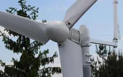 Montaż elektrowni wiatrowej w pobliżu drzew. Białe łopaty wirnika i gondola na tle błękitnego nieba.