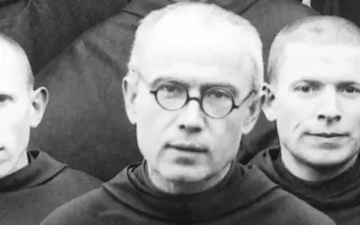 Trzej zakonnicy w habitach. W środku Maksymilian Kolbe w okularach. Ciekawostki o jego życiu i heroizmie.