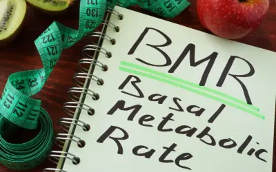 Notatnik z napisem BMR (Basal Metabolic Rate), obok jabłko, kiwi i miarka krawiecka. Obliczenia BMR, jak wzór Harrisa Benedicta, pomagają zrozumieć metabolizm.