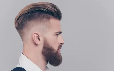 Mężczyzna z zarostem i fryzurą slick back, z wygolonymi bokami i dłuższymi włosami na górze.