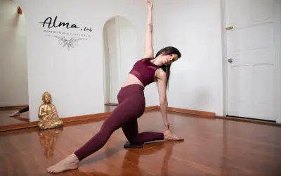 Mujer en postura de yoga, demostrando la fluidez del vinyasa yoga. Reflejo en espejo y Buda dorado.