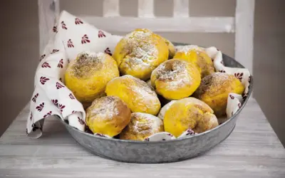 En skål med gyllene julgodis med saffran, pudrade med florsocker, på en duk med mönster.