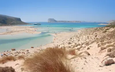 Piękne chania plaże z turkusową wodą, łagodnymi falami i piaszczystym wybrzeżem. W oddali widać statki wycieczkowe.
