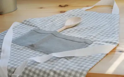 Gotowy fartuch kuchenny w kratkę, z drewnianą łyżką w kieszeni. Idealny poradnik, jak uszyć fartuch kuchenny.