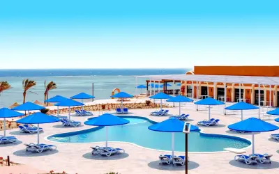 Basen z niebieskimi parasolami i leżakami, widok na morze. Idealne miejsce na wakacje, jak w Pickalbatros Portofino Marsa Alam.
