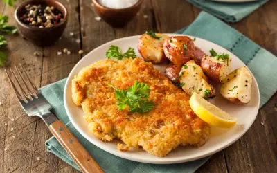 Goldbraunes Schnitzel, perfekt paniert, mit Rosmarinkartoffeln und Zitrone. So paniert man Schnitzel für ein köstliches Essen.