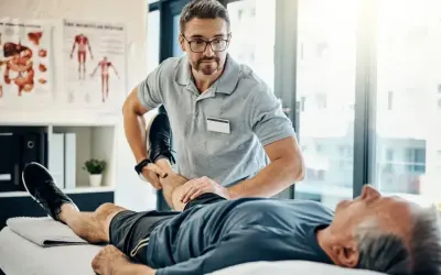 Fizjoterapeuta ćwiczy nogę starszego pacjenta. Rehabilitacja jest kluczowa, by dowiedzieć się, komu przysługuje szpital uzdrowiskowy.