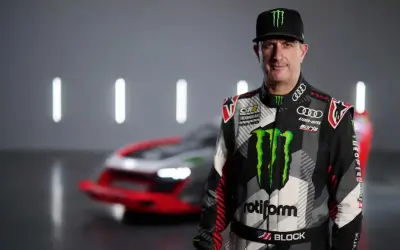 Ken Block, piloto de rally, posa con su traje de competición y un coche de Audi e-tron detrás.