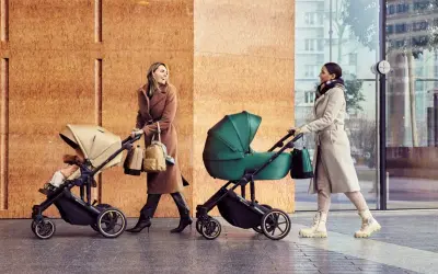 Dwie kobiety spacerują z wózkami Kinderkraft Route. Jedna w beżowym płaszczu, druga w jasnym.