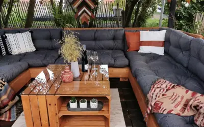 Gemütliches Palettensofa bauen: Eine Lounge-Ecke im Garten mit Glas-Couchtisch, Kissen und Decken. Perfekt für entspannte Stunden.