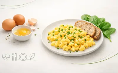 Jajecznica na talerzu z pieczywem i szpinakiem, obok surowe jajka.