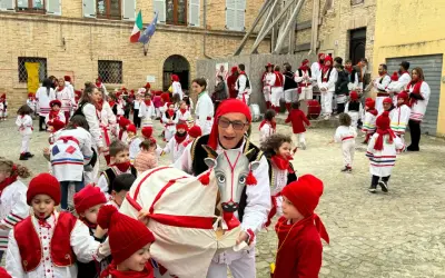 Un uomo con un costume da toro guida una sfilata di bambini vestiti di rosso e bianco per il carnevale nelle Marche.