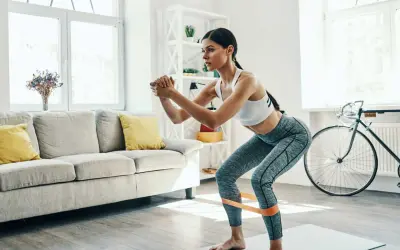 Femme faisant des squats avec une bande de résistance pour affiner ses jambes, dans un salon lumineux.