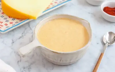 Crema de salsa de queso lista para servir, con un trozo de queso y especias al fondo.