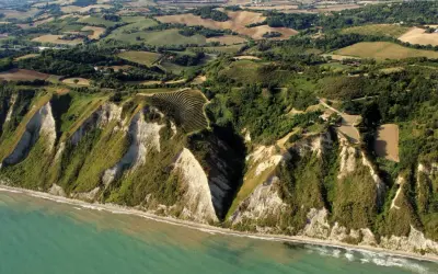 Scogliere a picco sul mare turchese a Gabicce Mare, Marche. Campi coltivati e vegetazione rigogliosa adornano le colline retrostanti.
