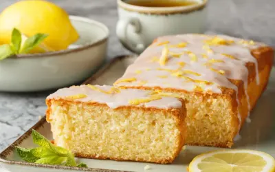 Pyszna babka cytrynowa z lukrem i skórką cytrynową, udekorowana miętą i plasterkiem cytryny. Idealna na podwieczorek.
