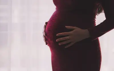 Ciężarna kobieta w czerwonej sukience obejmuje brzuch. Dylematy związane z umową zlecenie a ciążą.