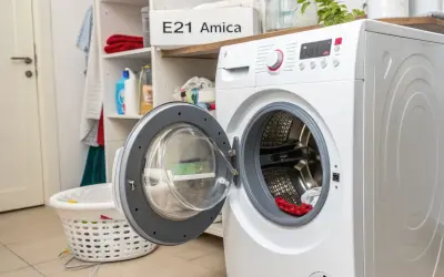 Pralka Amica z otwartymi drzwiczkami, na półce widoczny napis "E21 Amica", sugerujący błąd. Obok kosz na pranie.