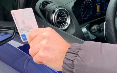 Mano sujetando permiso de conducir español dentro de un coche moderno, anticipando la conducción autónoma en España.