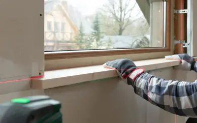 Montaż nowego parapetu wewnętrznego w bloku. Czerwona linia lasera pomaga w precyzyjnym ułożeniu drewnianego elementu.