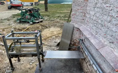 Baustelle mit Bagger, Maschine und Metallkonstruktion. Eine horizontale Sperrschicht aus Metallblech schützt die Ziegelwand.