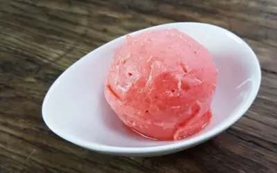 Ein Löffel cremiges Erdbeereis mit Sahne in einer weißen Schale auf Holzhintergrund.