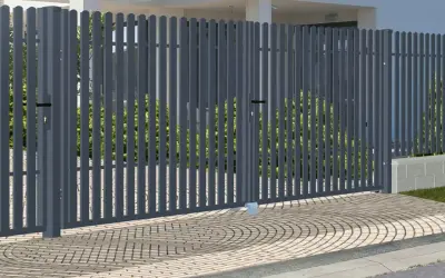 Nowoczesna, szara brama do ogrodzenia panelowego, z dwoma skrzydłami, otwiera drogę do zadbanego ogrodu.