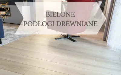 Jasne, bielone drewno na podłodze w salonie, z widocznym fragmentem granatowej kanapy i różowego fotela.