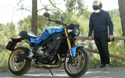 Motocicleta azul de estilo neo retro con detalles dorados, aparcada junto a un hombre con casco.