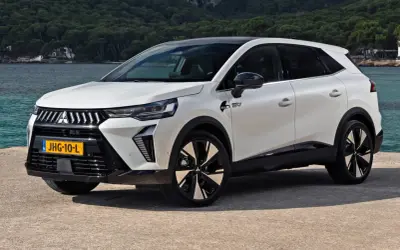 Nowy model Mitsubishi, biały SUV z czarnym dachem, stoi nad wodą. Nowoczesne linie i felgi podkreślają jego dynamiczny charakter.
