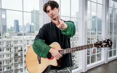 Młody muzyk z gitarą, pozdrawia gestem pokoju. Może właśnie tworzy nowe, popularne piosenki.