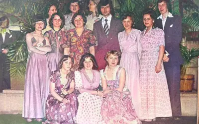 Grupa osób w eleganckich, pastelowych kreacjach. Widać długie suknie i garnitury, typowe dla lat 60 stylizacje.
