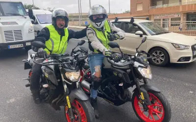 Dos motoristas con chalecos reflectantes y cascos posan con sus motos. Uno hace un gesto de "pulgar arriba". ¡Listos para la aventura en su a1 de moto!