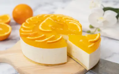 Sernik pomarańczowy z mascarpone, ozdobiony plasterkami pomarańczy, wygląda apetycznie. Kawałek ciasta został już odkrojony.
