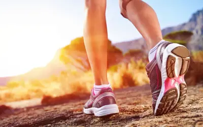 Nogi w butach sportowych stawiają kolejne kroki na kamienistej ścieżce. Słońce zachodzi za górami, tworząc ciepłą, złotą poświatę. Ile to 10000 kroków?