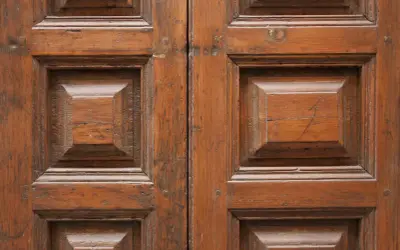 Renowacja drzwi drewnianych cennik: zbliżenie na zabytkowe, dwuskrzydłowe drzwi z widocznymi panelami i naturalnym usłojeniem drewna.
