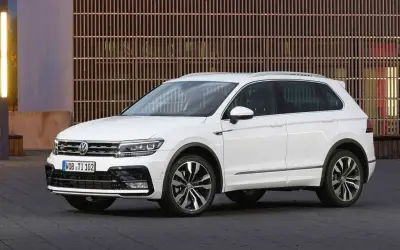 Biały Volkswagen Tiguan 2019 z eleganckimi felgami stoi przed nowoczesnym budynkiem z drewnianą fasadą.