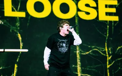 Wokalista z otwartymi ustami śpiewa do mikrofonu na tle sceny z napisem "LOOSE".
