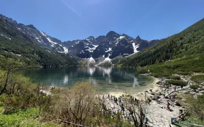Widok na Morskie Oko z górami w tle i turystami na brzegu.