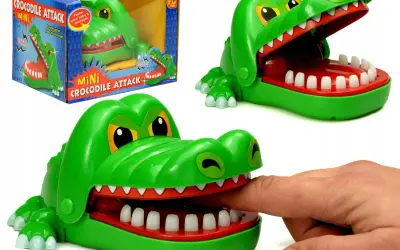 Zielona zabawka gra krokodyl z otwartą paszczą, do której włożono palec. Obok pudełko z napisem "Mini Crocodile Attack".