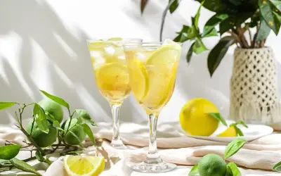Dwa kieliszki orzeźwiającego likieru cytrynowego limoncello z lodem i plasterkami cytryny, otoczone świeżymi cytrynami i limonkami.