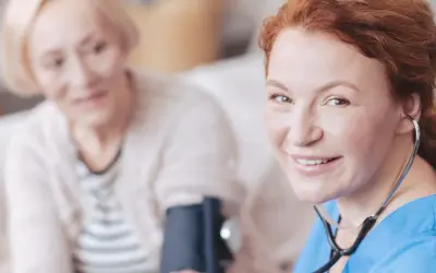 Uśmiechnięta pielęgniarka z rudymi włosami mierzy ciśnienie starszej kobiecie. Dopegyt w ciąży jest bezpieczny dla matki i dziecka.