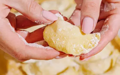 Dłonie z pudrowym cukrem delikatnie formują pyszne pierogi z serem.